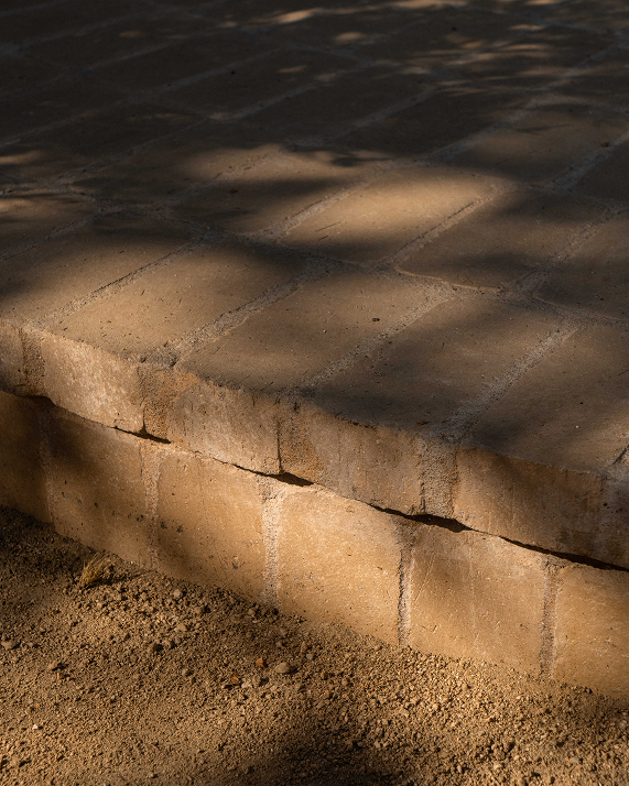 A close-up outdoor shot of tan stone pavers as steps with dappled sunlight and shadows cast across the surface.