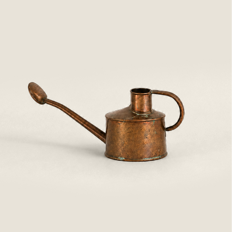 A small vintage copper watering can with a long spout and side handle, photographed on a plain light beige background.