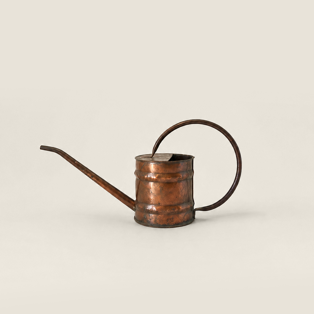 A copper watering can with a long spout and a loop handle, shown on a plain light beige background.