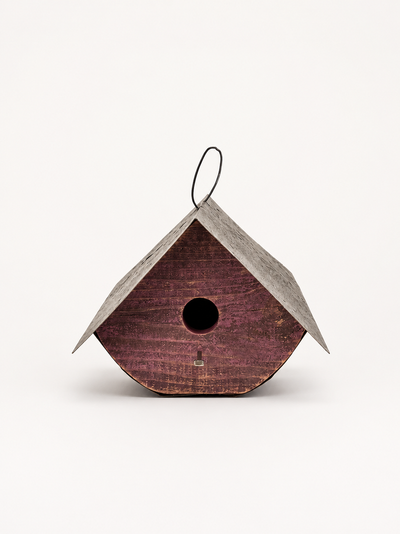 A rustic wooden birdhouse with a pointed gray metal roof, a hanging loop, and a round entrance hole, shown against a plain white background.