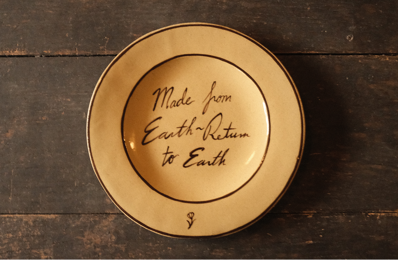 Ceramic plate with "made from earth, return to earth" inscribed text on a wooden surface