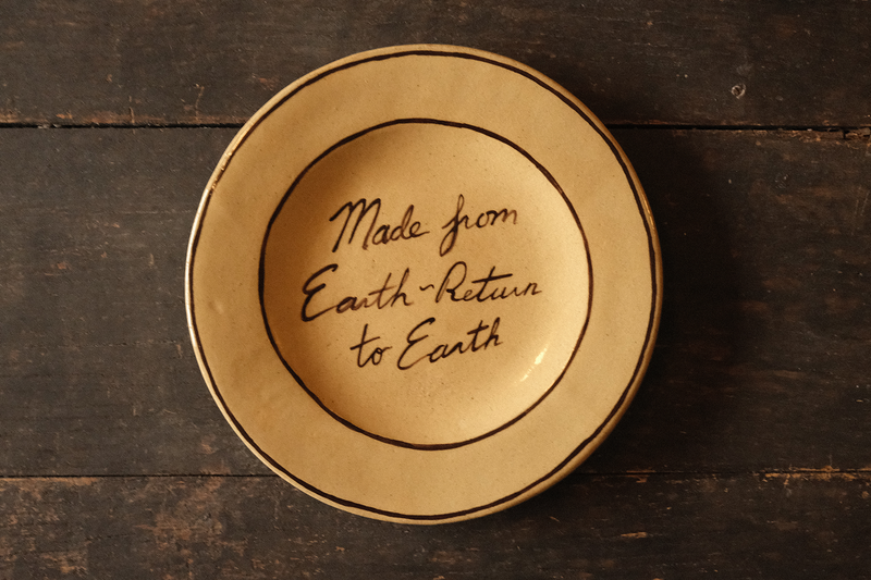 Ceramic plate with "made from earth, return to earth" inscribed text on a wooden surface