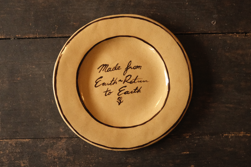 Ceramic plate with "made from earth, return to earth" inscribed text on a wooden surface