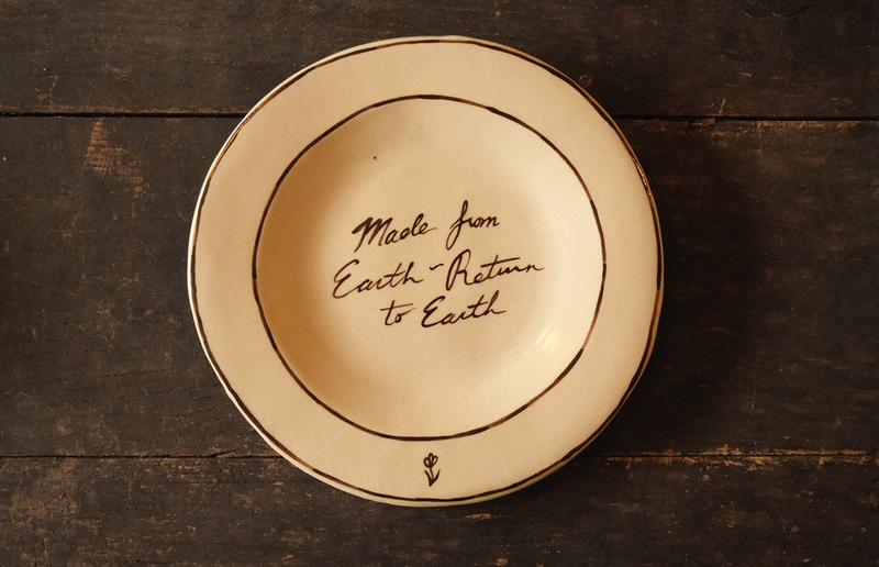 Ceramic plate with "made from earth, return to earth" inscribed text on a wooden surface
