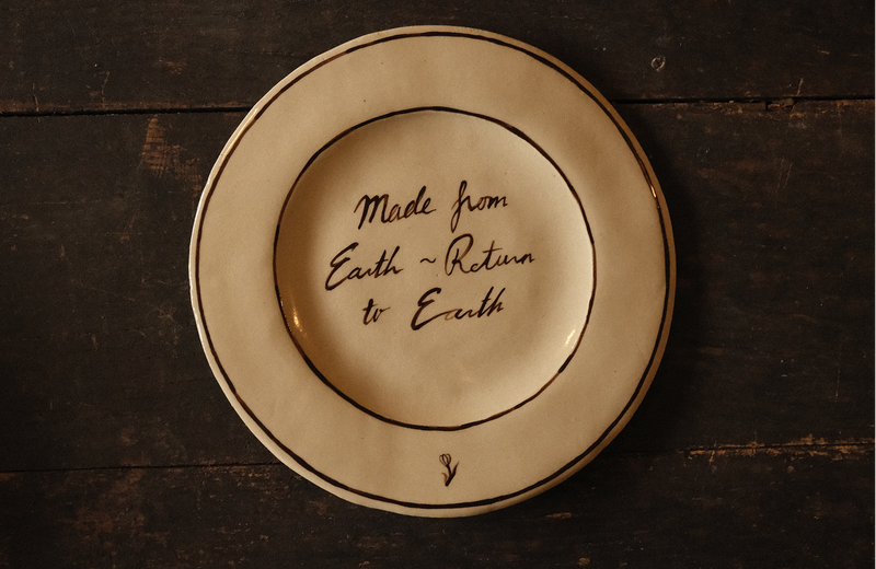 Ceramic plate with "made from earth, return to earth" inscribed text on a wooden surface