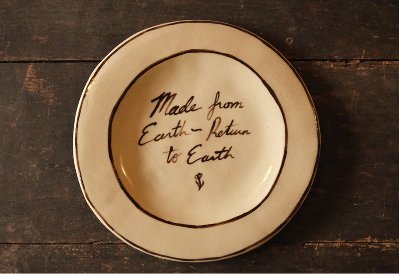 Ceramic plate with "made from earth, return to earth" inscribed text on a wooden surface