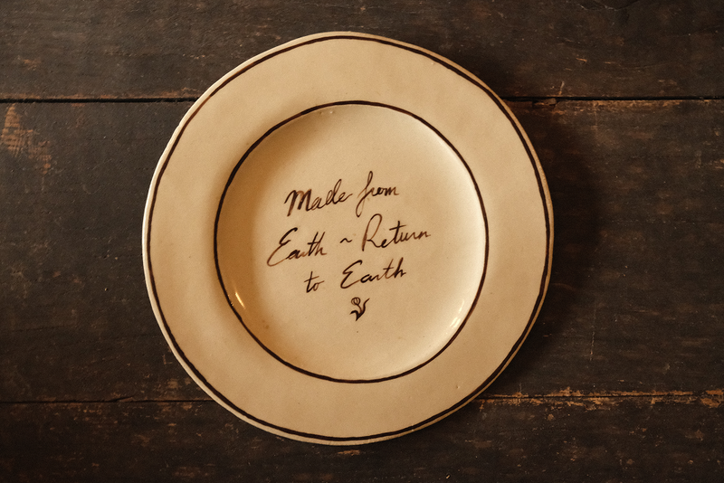 Ceramic plate with "made from earth, return to earth" inscribed text on a wooden surface