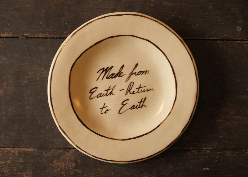 Ceramic plate with 'Made from Earth, Return to Earth' text on a wooden surface