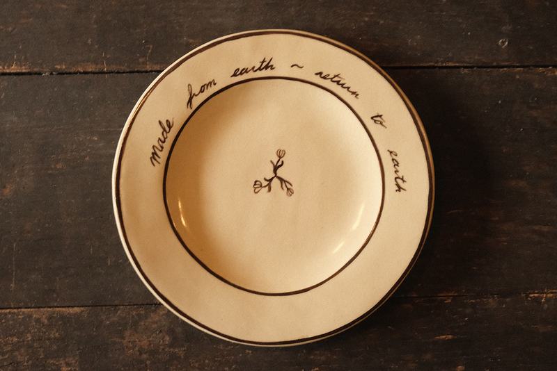 Ceramic plate with "made from earth, return to earth" inscribed text on a wooden surface