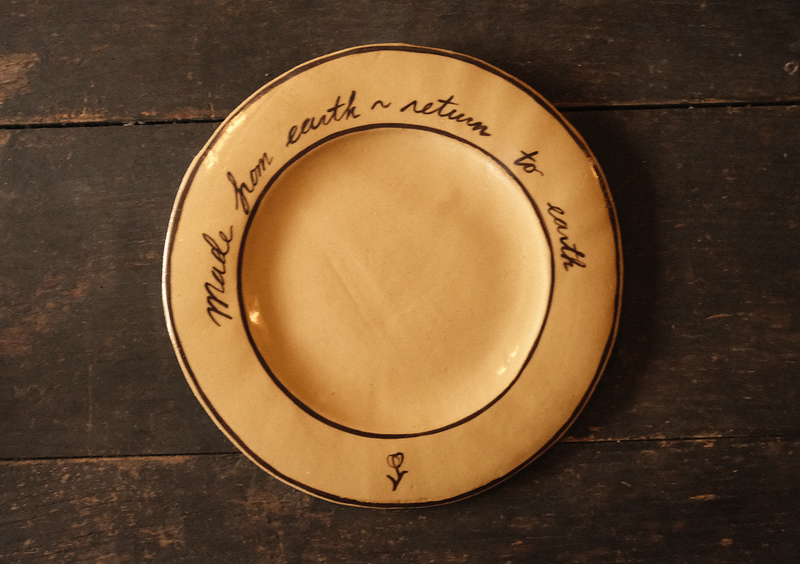 Ceramic plate with "made from earth, return to earth" inscribed text on a wooden surface
