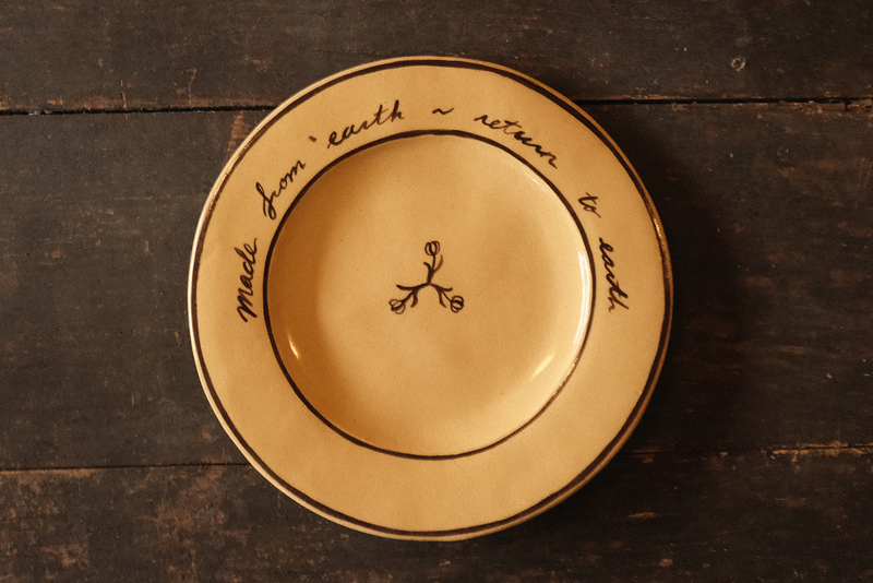 Ceramic plate with "made from earth, return to earth" inscribed text on a wooden surface