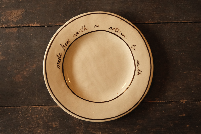 Ceramic plate with "made from earth, return to earth" inscribed text on a wooden surface