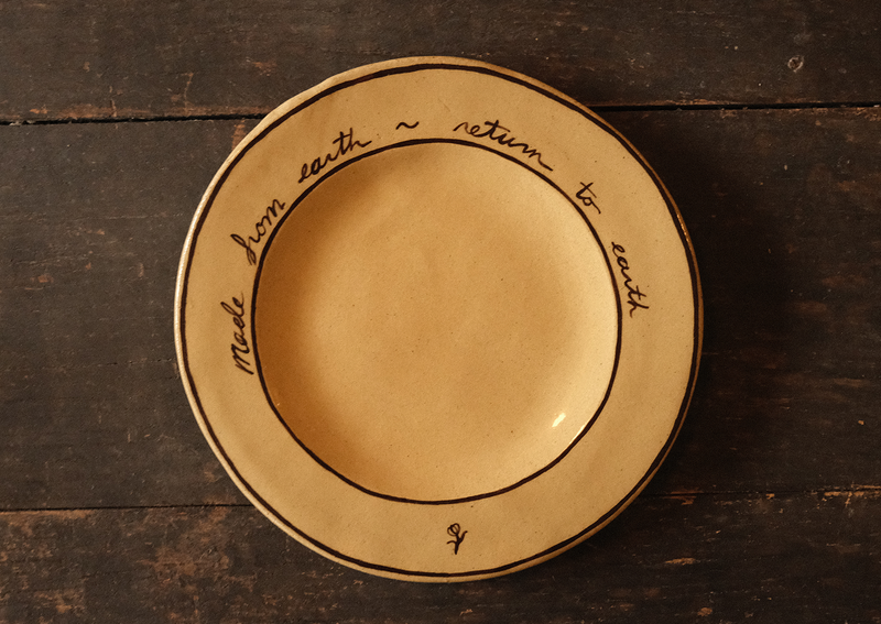 Ceramic plate with "made from earth, return to earth" inscribed text on a wooden surface