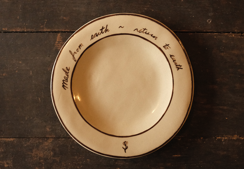 Ceramic plate with "made from earth, return to earth" inscribed text on a wooden surface