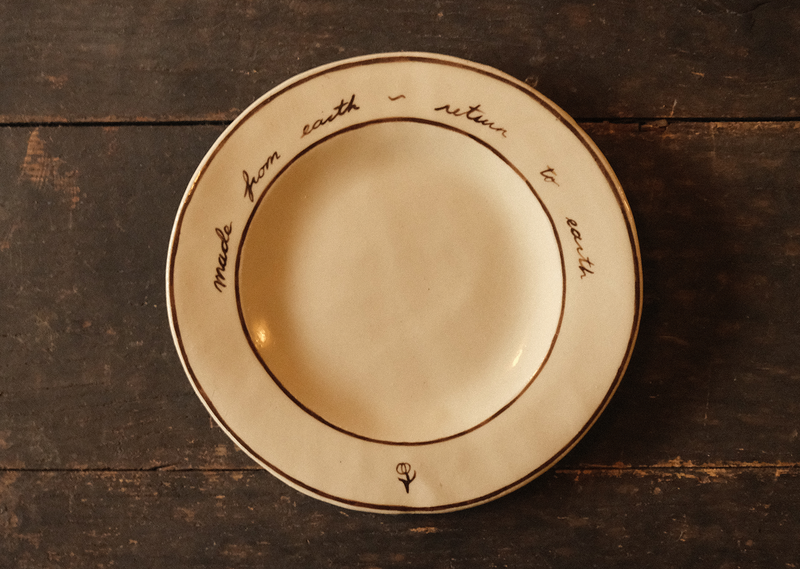 Beige ceramic plate with "made from earth, return to earth" inscribed text on a wooden surface