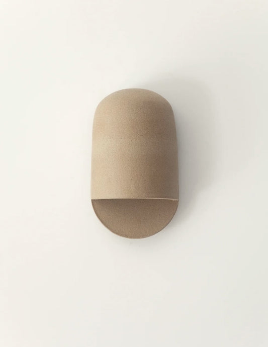 A minimalist, dome-shaped wall sconce in a natural light brown wood finish, mounted on a plain white wall.