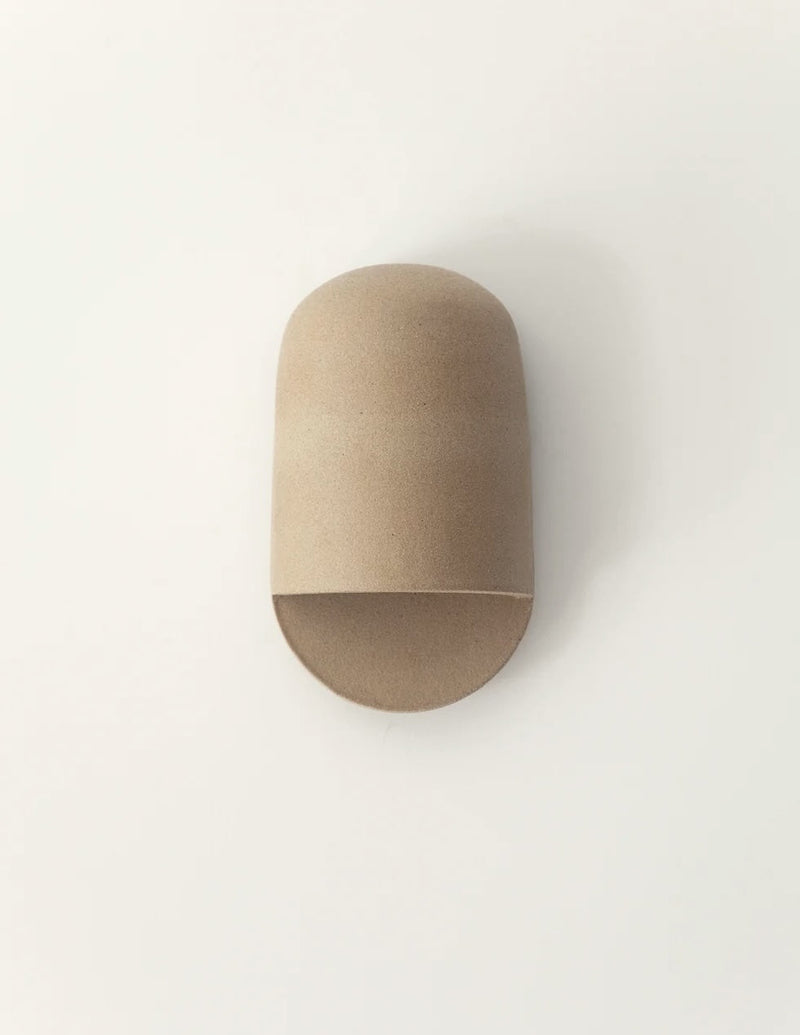 A minimalist, dome-shaped wall sconce in a natural light brown wood finish, mounted on a plain white wall.