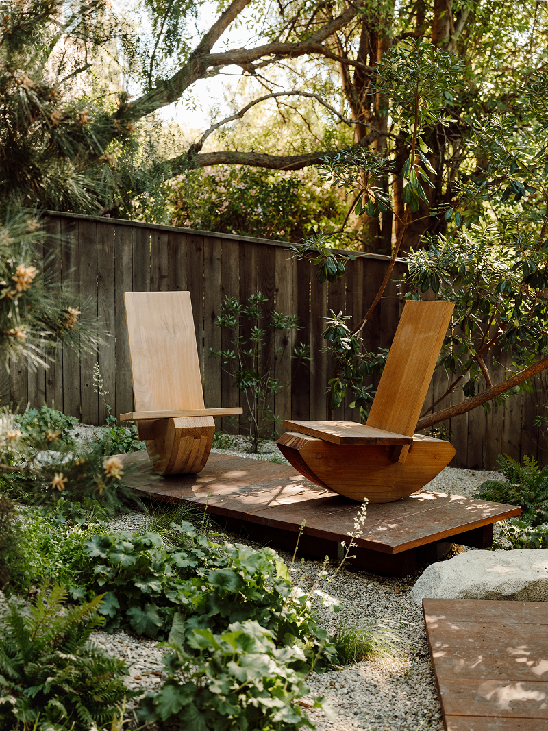 Wooden chairs on a platform surrounded by greenery and a wooden fence.
