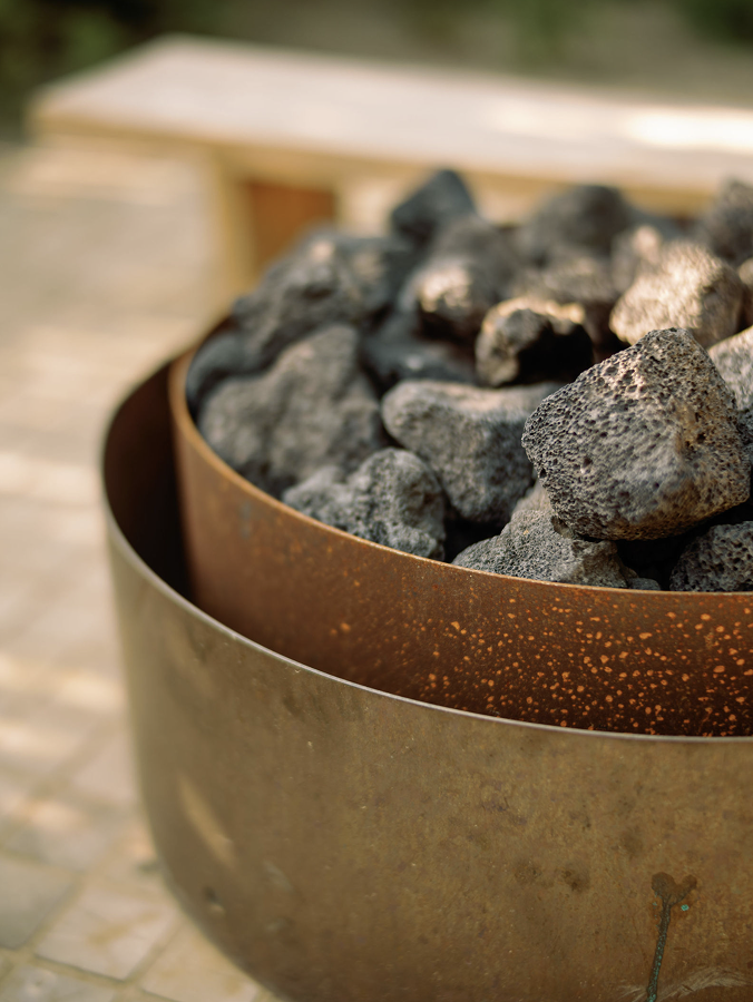 Metal fire pit with volcanic rocks inside on a blurred outdoor background