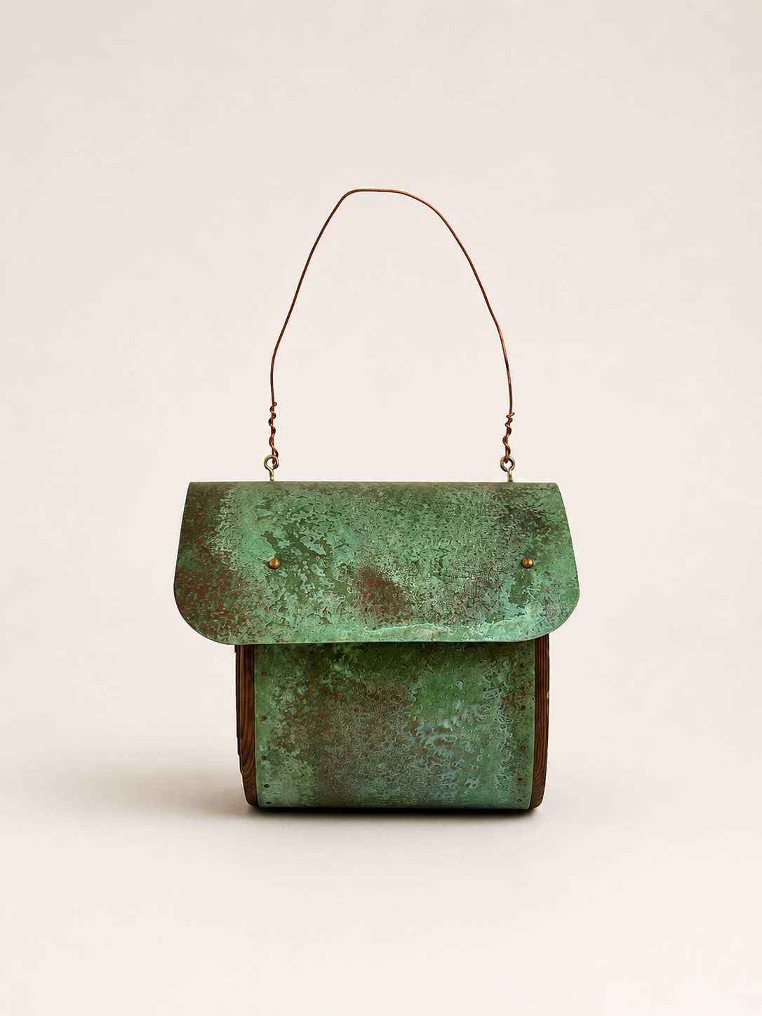 A small structured birdhouse with a distressed green patina finish and a thin brown top handle, photographed against a plain light beige background.