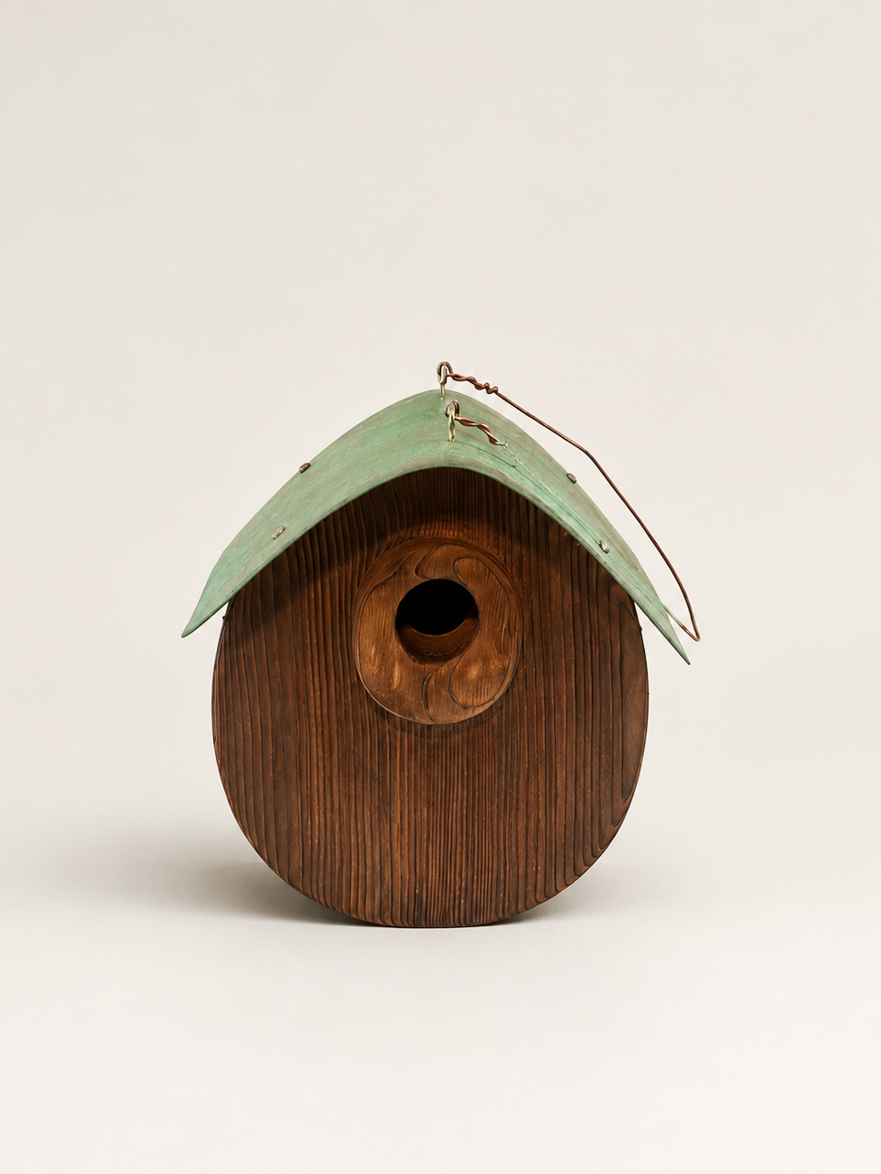 A rustic wooden birdhouse with a dark brown wood-grain body and a weathered light green metal roof, featuring a small hanging wire loop at the top.