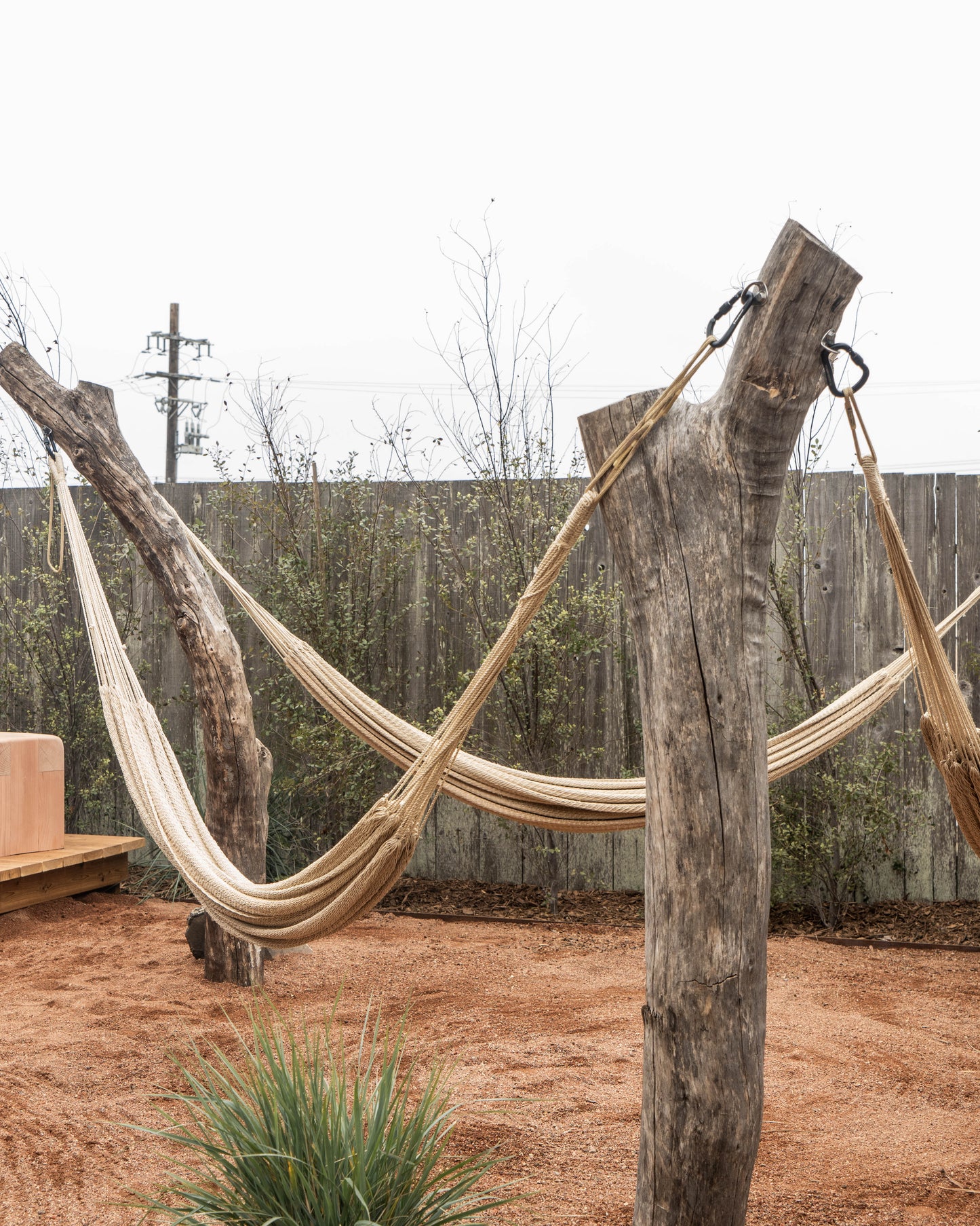 Hammock hanging between two wooden posts in an outdoor setting with a fence and plants in the background.