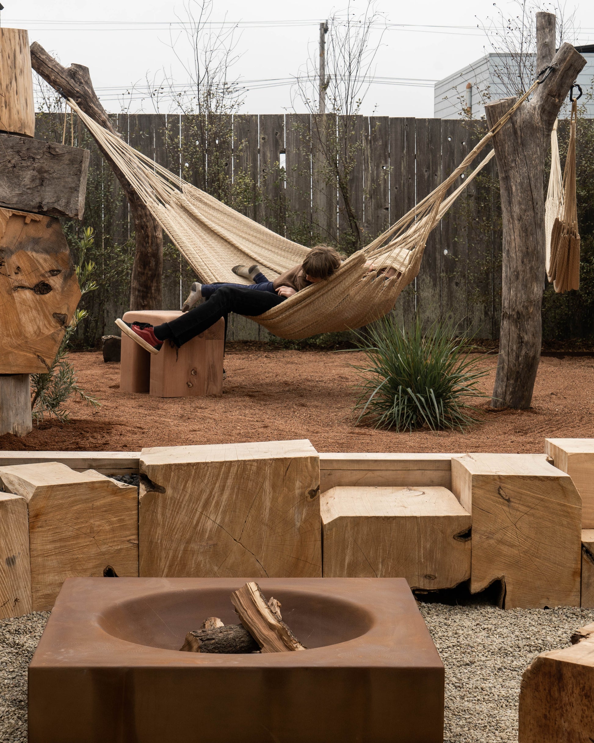 Outdoor setting with wooden furniture, fire pit, and person in a hammock.