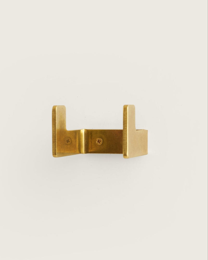 A brass small utility hook mounted on a white wall.