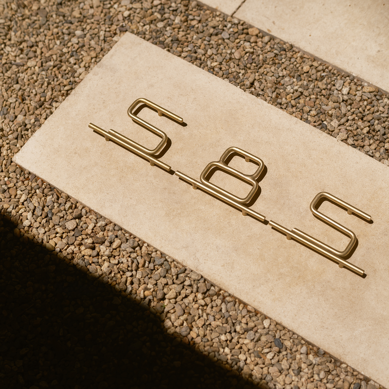 Brick with 'SBS' brass house numbers on a textured surface