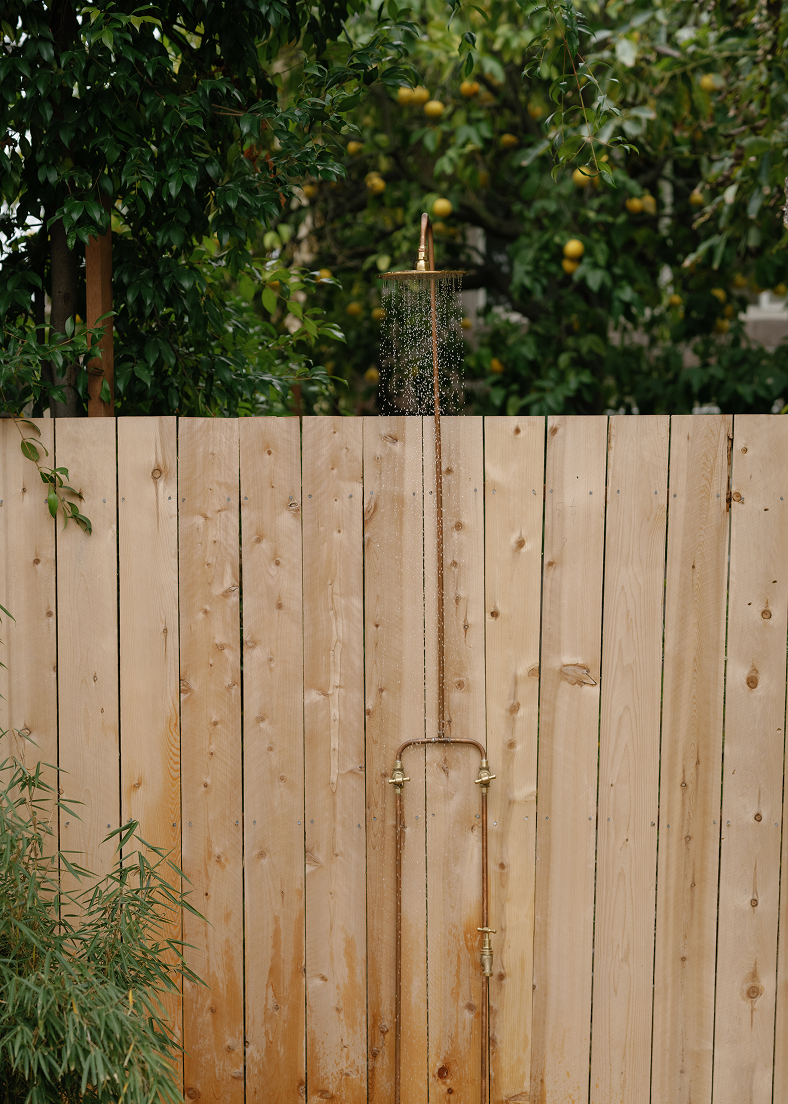 Outdoor shower mounted on a wooden fence with trees in the background