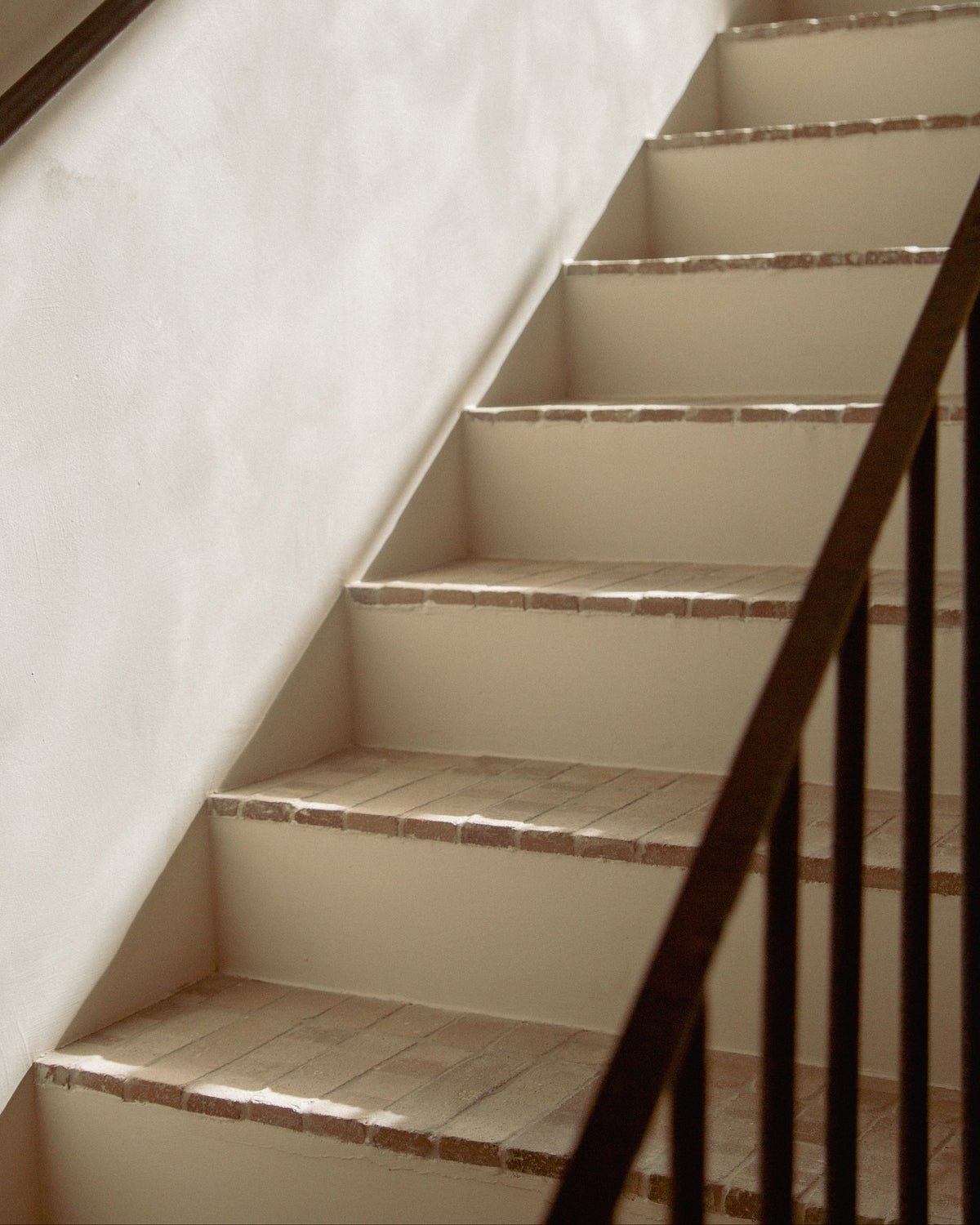 An interior staircase with cream-colored steps and walls, bordered by a dark brown wooden railing.