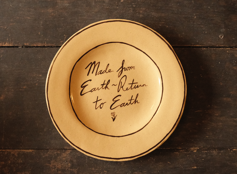 Ceramic plate with "made from earth, return to earth" inscribed text on a wooden surface