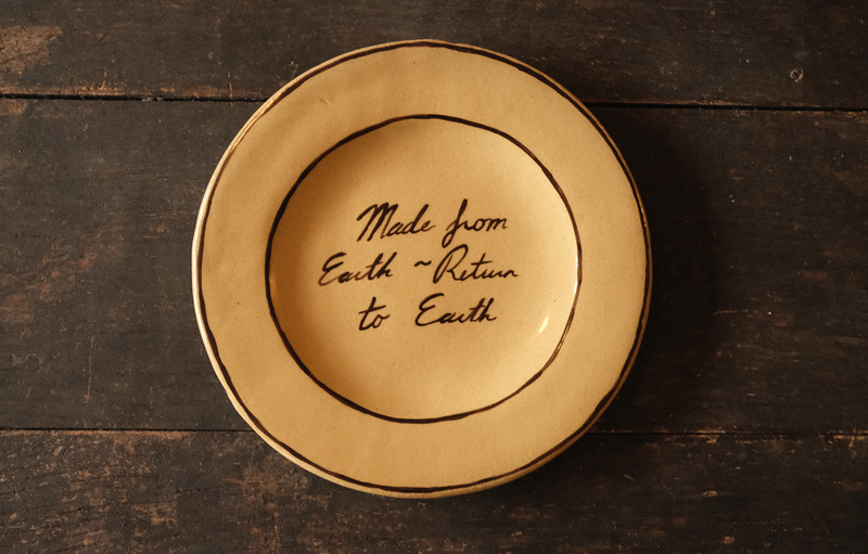 Ceramic plate with "made from earth, return to earth" inscribed text on a wooden surface