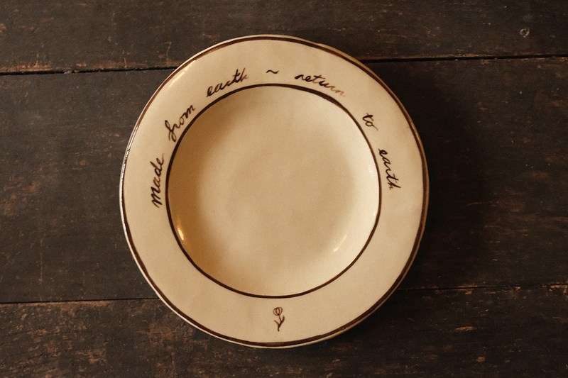 Ceramic plate with "made from earth, return to earth" inscribed text on a wooden surface