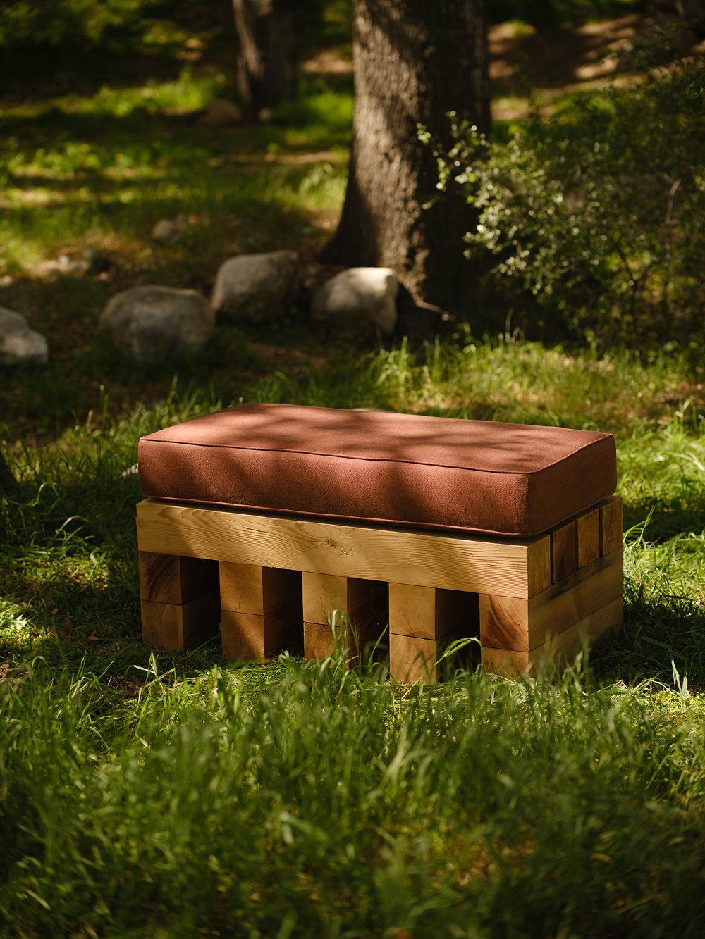 Wooden ottoman with a cushion in a grassy outdoor setting