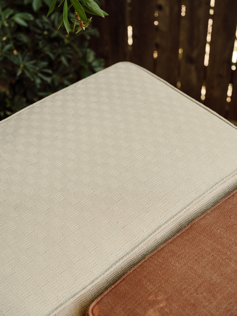 Close-up of a beige fabric surface with a brown border, possibly part of outdoor furniture.