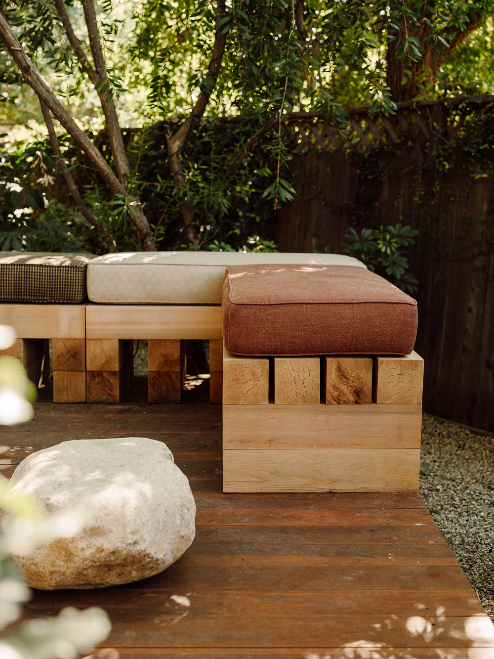 Wooden outdoor seating with cushions on a wooden deck surrounded by greenery
