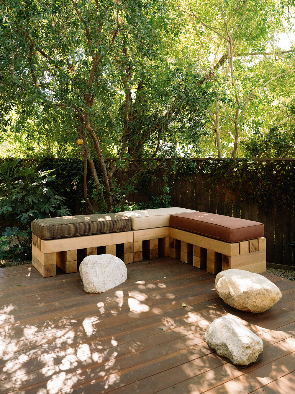 Outdoor seating area with wooden bench and cushions on a wooden deck, surrounded by trees.