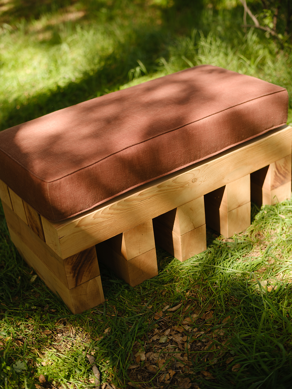 Wooden bench with a brown cushion on a grassy background