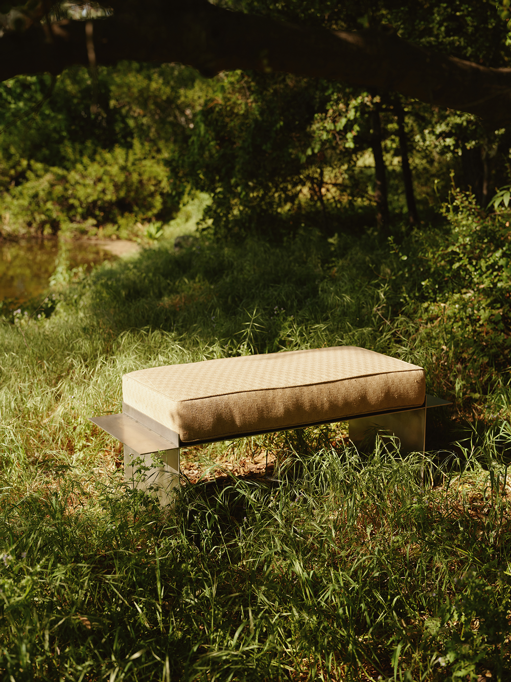 metal bench in a grassy outdoor setting with trees and water in the background