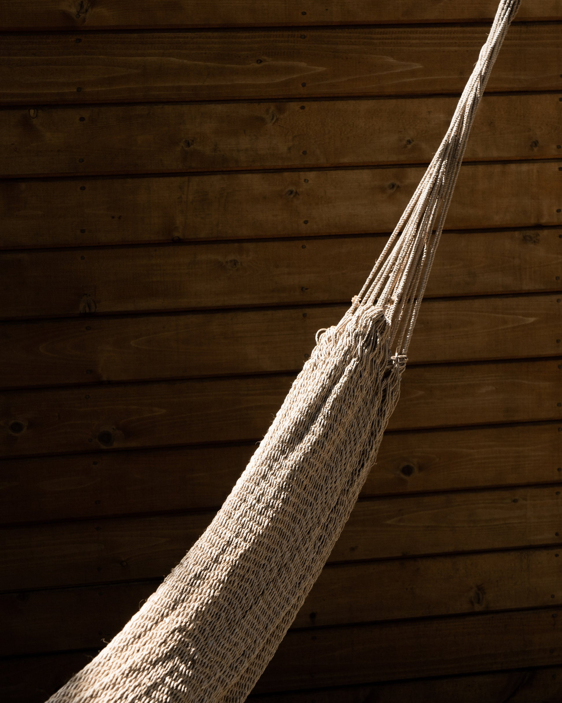 Textured beige hammock hanging against a wooden wall